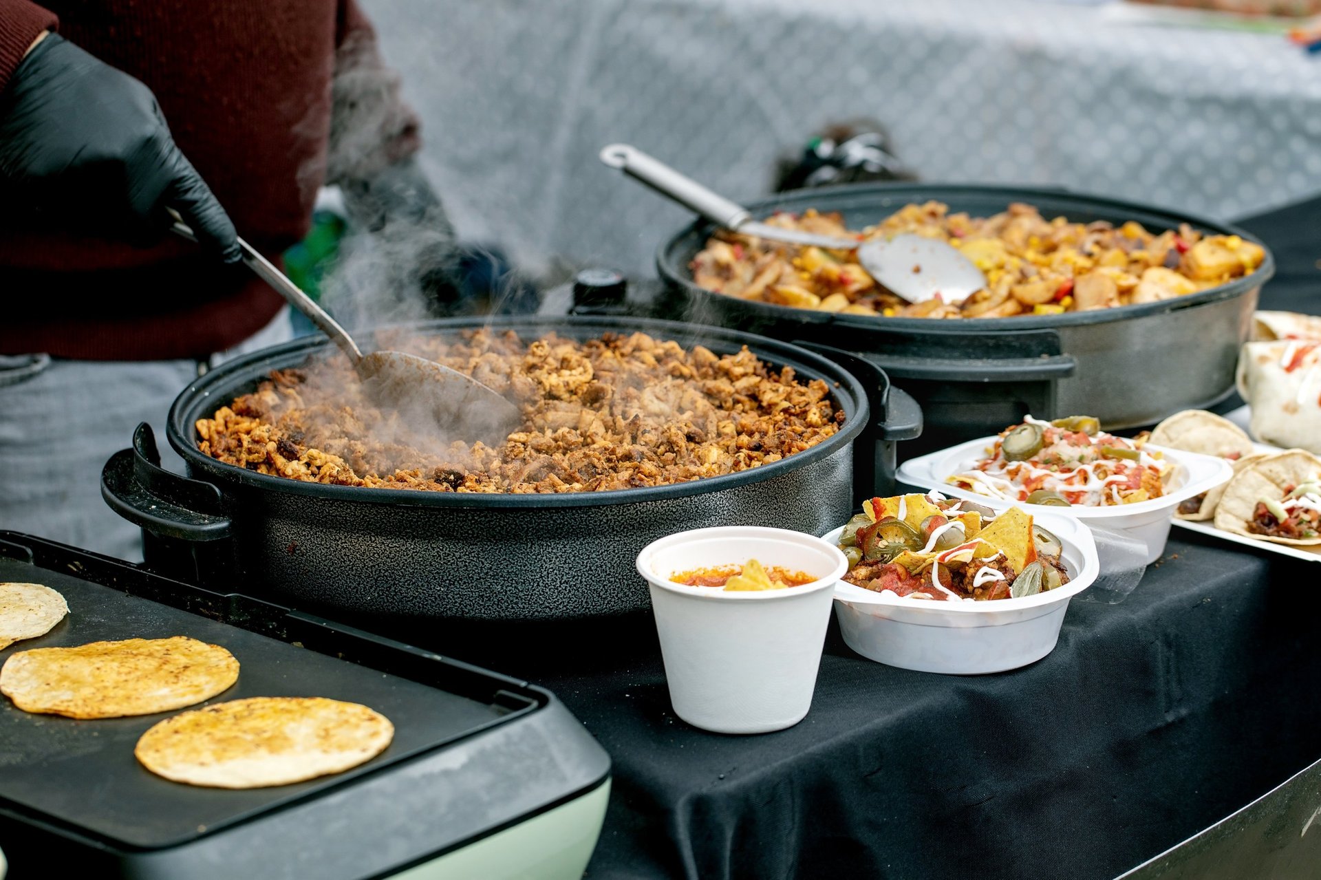 Mexican street food preparation with cook stirring meat in cast iron pan